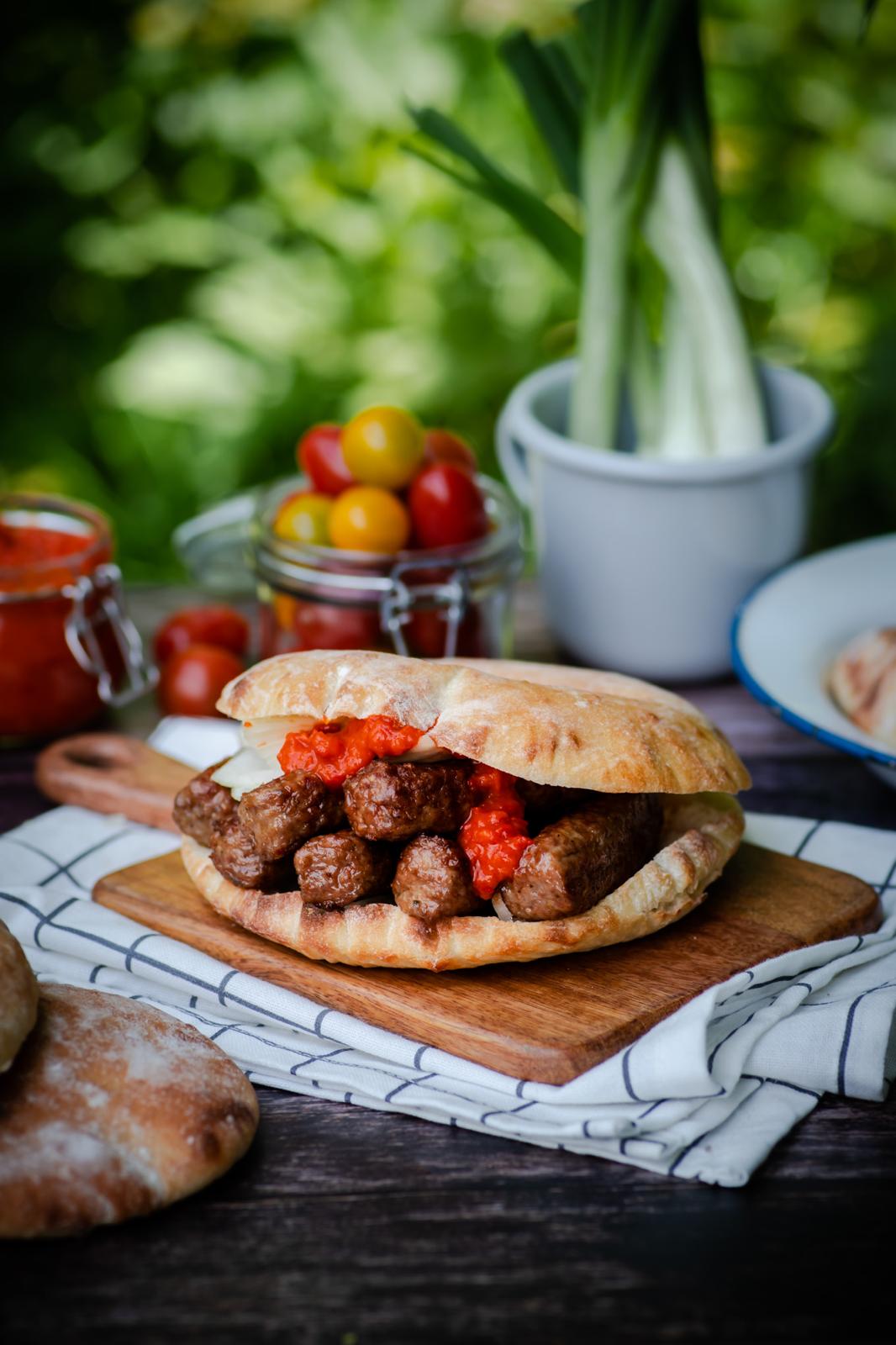 Ćevapčići im frischen Fladenbrot mit Ajvar und Zwiebeln im Grünen serviert